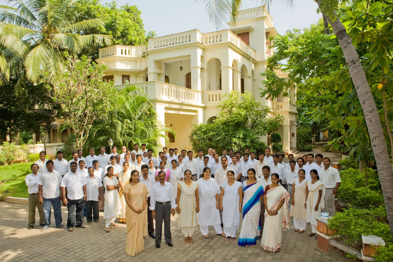 Full-staff group photograph of around seventy employees in white uniforms, arranged in rows outside their office building