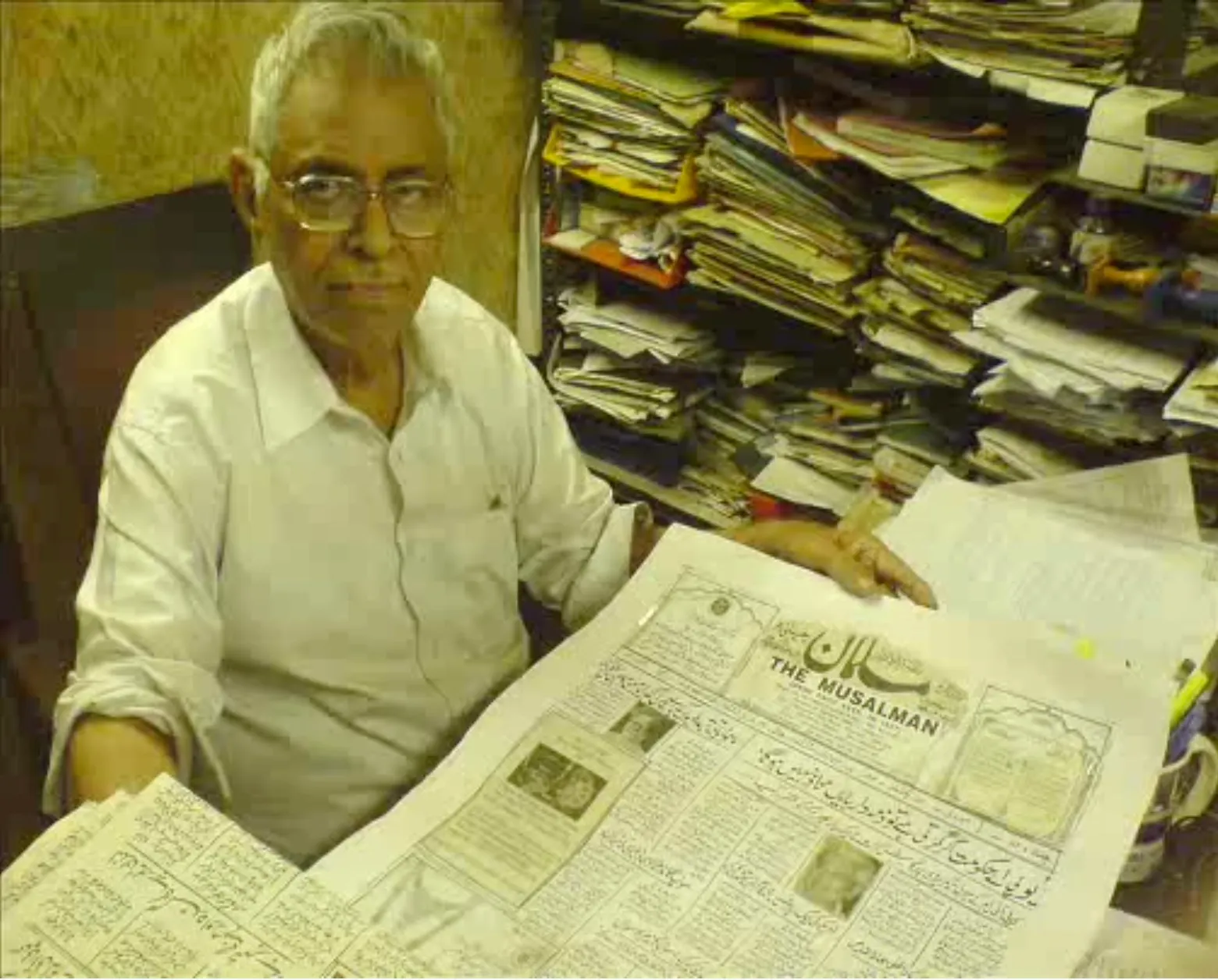 Mr. Syed Fazlulla, editor of The Musalman, at his desk holding a hand-calligraphed copy of the newspaper